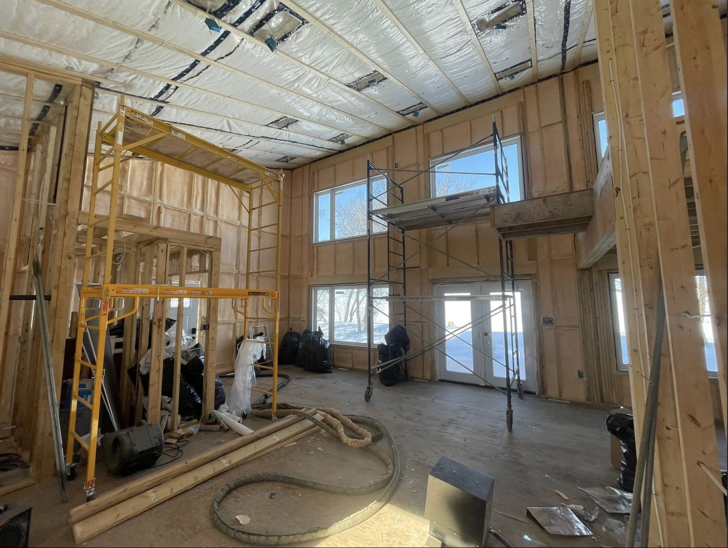 Two-storey great room under construction with spray foamed walls and snow visible through the windows