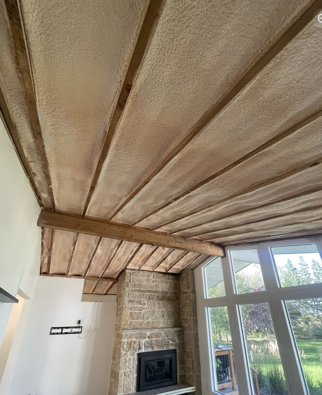 Vaulted sunroom ceiling spray foamed between wood rafters above a stone fireplace and large windows